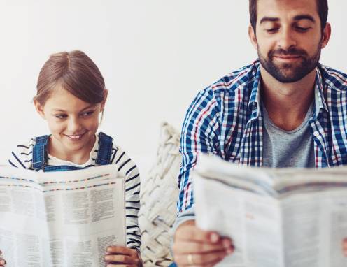 Mann und Tochter lesen nebeneinander Zeitung